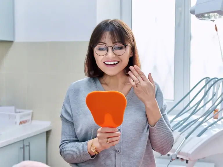 A patient looking at her new smile in a hand mirror